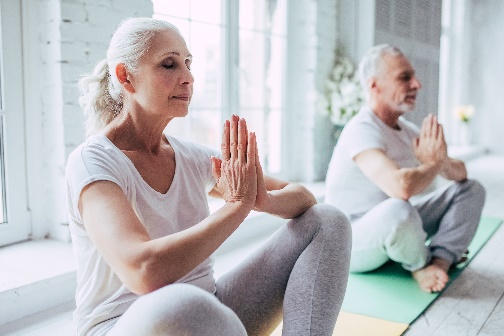 A senior man and woman sit on yoga mats in a bright, sunlit room, practicing meditation - https://wmderma.com/